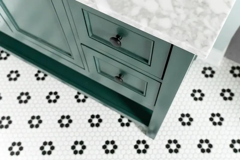 Detail of hunter green bathroom vanity with marble countertop and black penny tile floor in a Minnesota bathroom remodel