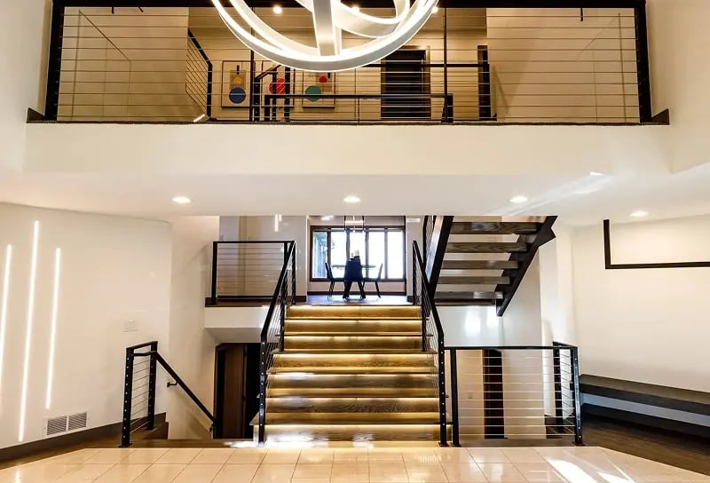 Minnesota commercial remodel with dramatic open staircase, LED-lit wood treads, cable railings, and circular chandelier