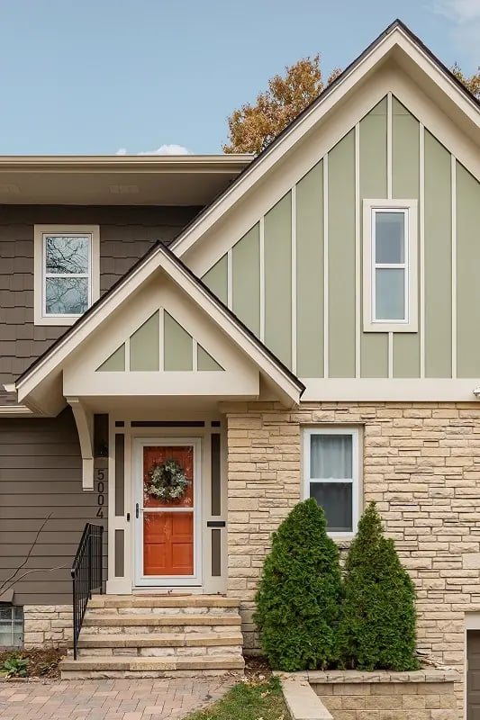 Minnesota home addition exterior with sage green board and batten gable, stone base, and craftsman entry door