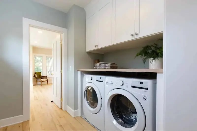 Custom laundry nook in a Minnesota home addition with white upper cabinets, butcher block shelf, and side-by-side washer and dryer