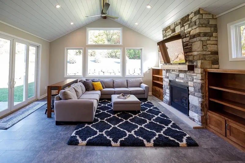 Minnesota home addition with vaulted shiplap ceiling, stone fireplace, and wall of windows overlooking backyard
