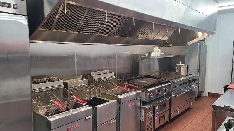 Commercial kitchen installation with stainless steel cooking equipment and exhaust hood