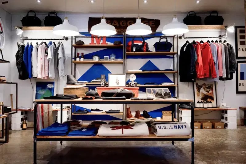 Retail store build-out with open shelving, clothing displays, and industrial pendant lighting by Titus Contracting