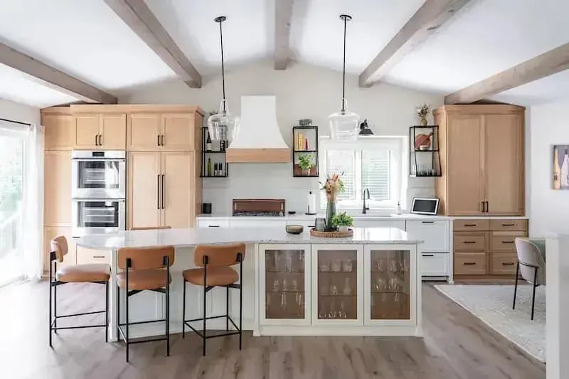 Open-concept kitchen remodel with natural wood cabinets, vaulted ceiling with exposed beams, and large island by Titus Contracting