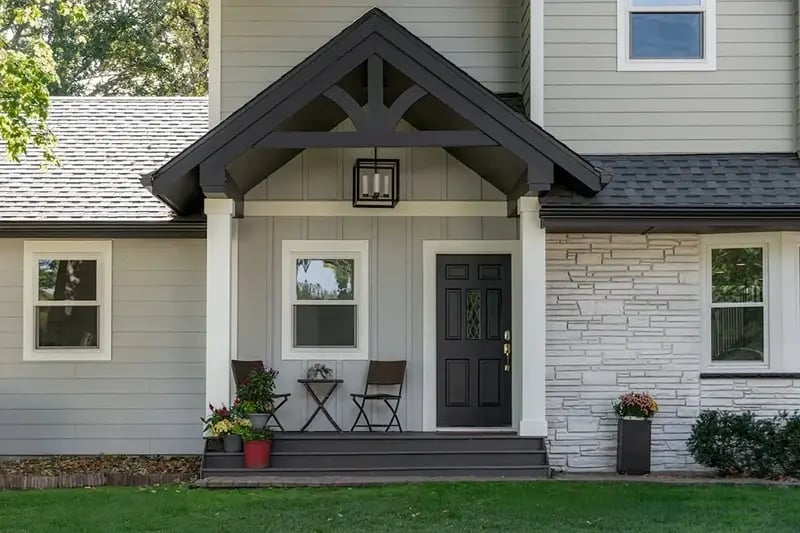Minnesota home addition with craftsman gable entry, exposed timber trusses, black front door, and stacked stone accent