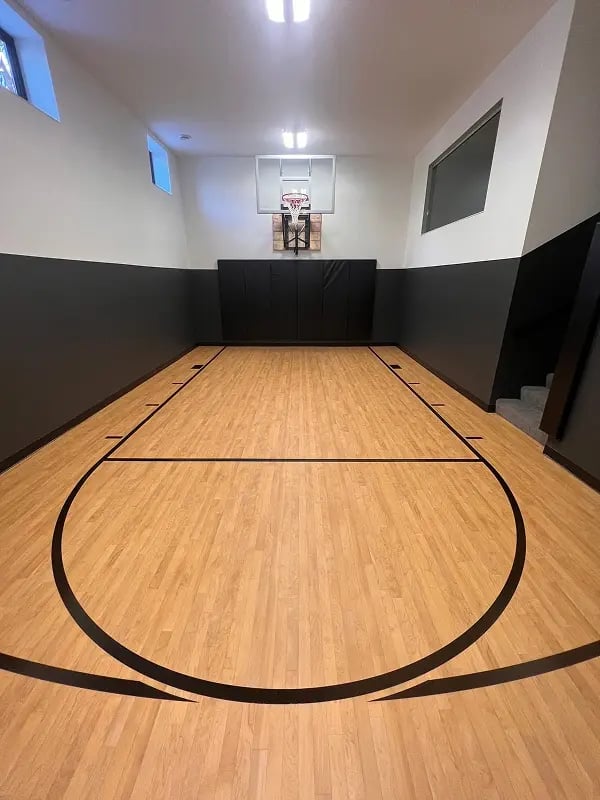 Completed indoor basketball court with hardwood sport floor, wall padding, and backboard in a Minnesota home
