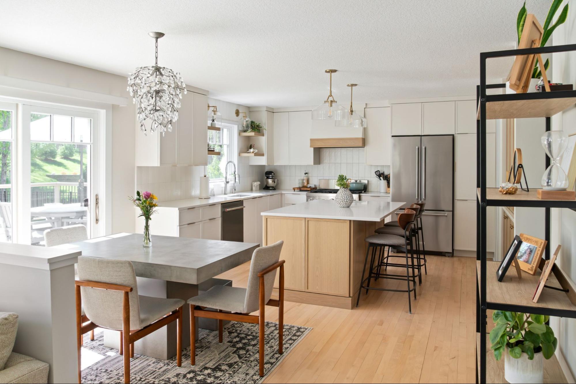 a kitchen with a small dining area. the kitchen is airy and light, with white walls and cream cabinets. open shelving includes several plants. ample natural light.