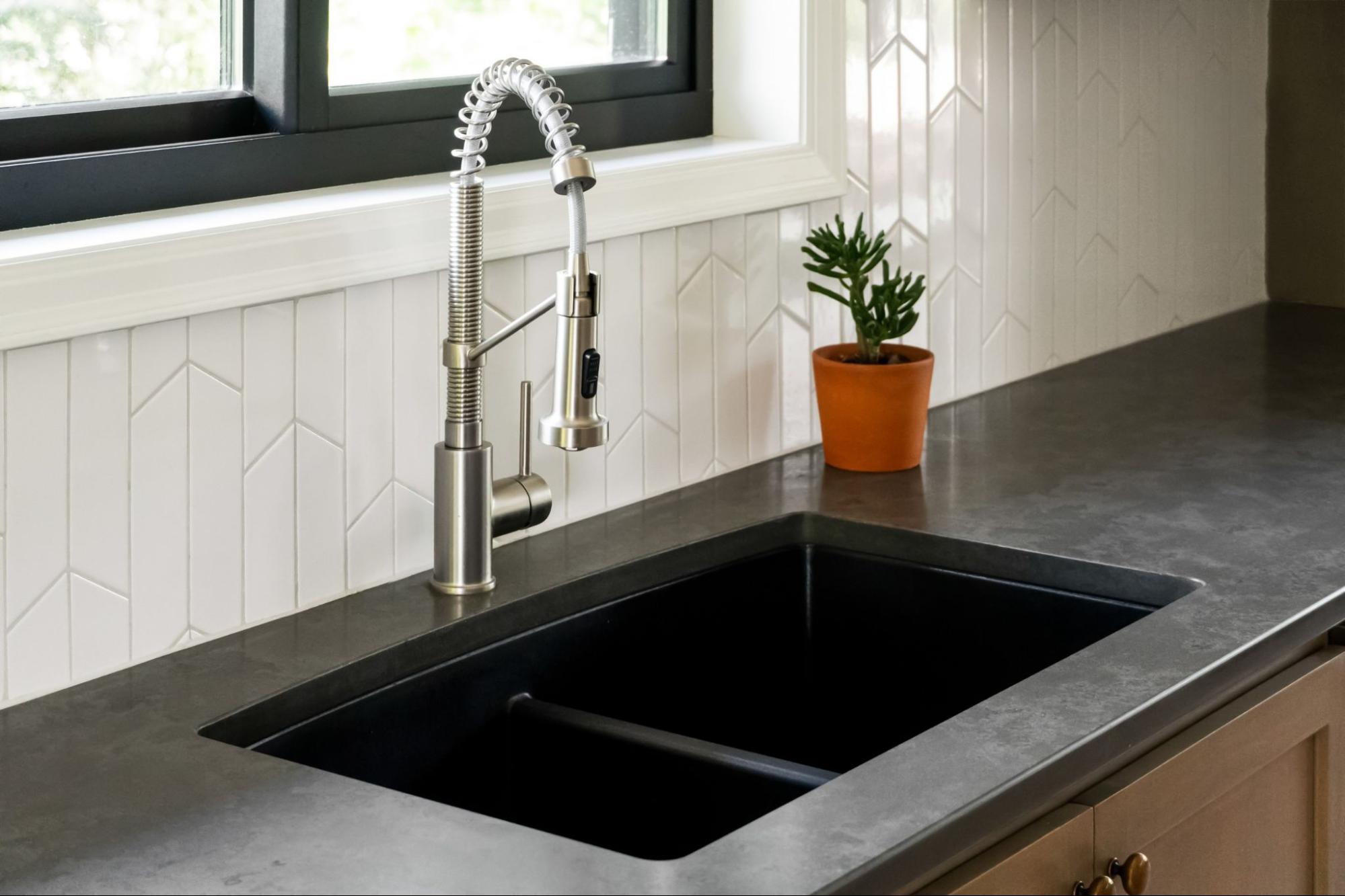 close-up of a double kitchen sink inside a dark gray countertop. the detachable faucet offers many spray options.