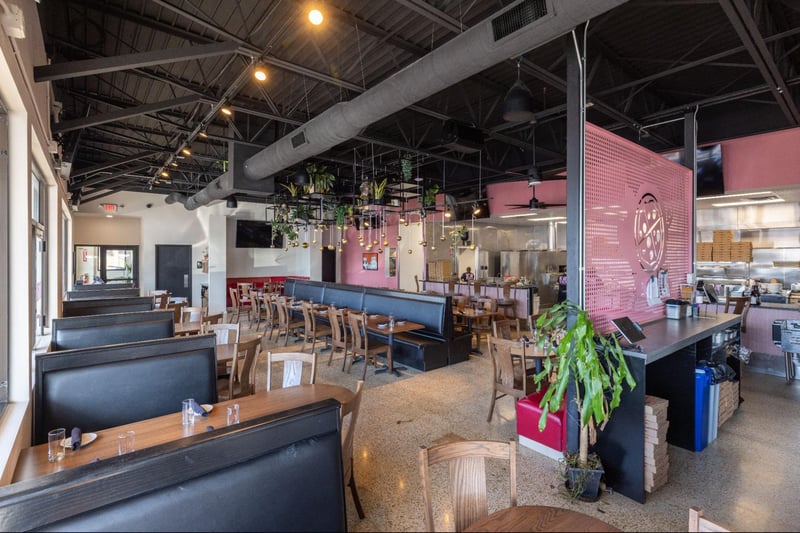 Spacious restaurant dining area with booth seating, open kitchen, and hanging plants with decorative lighting