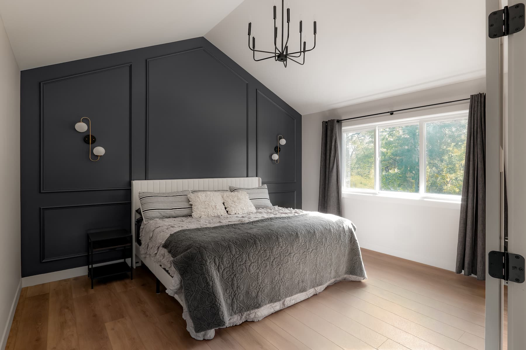 bedroom with gorgeous navy accent wall featuring wainscoting and bespoke midcentury-inspired wall sconces.