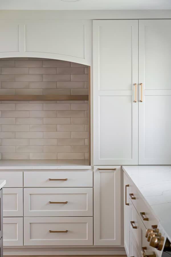 an archway above a countertop inside of a kitchen. warm cream tiles and golden accents create a backsplash underneath the arch.