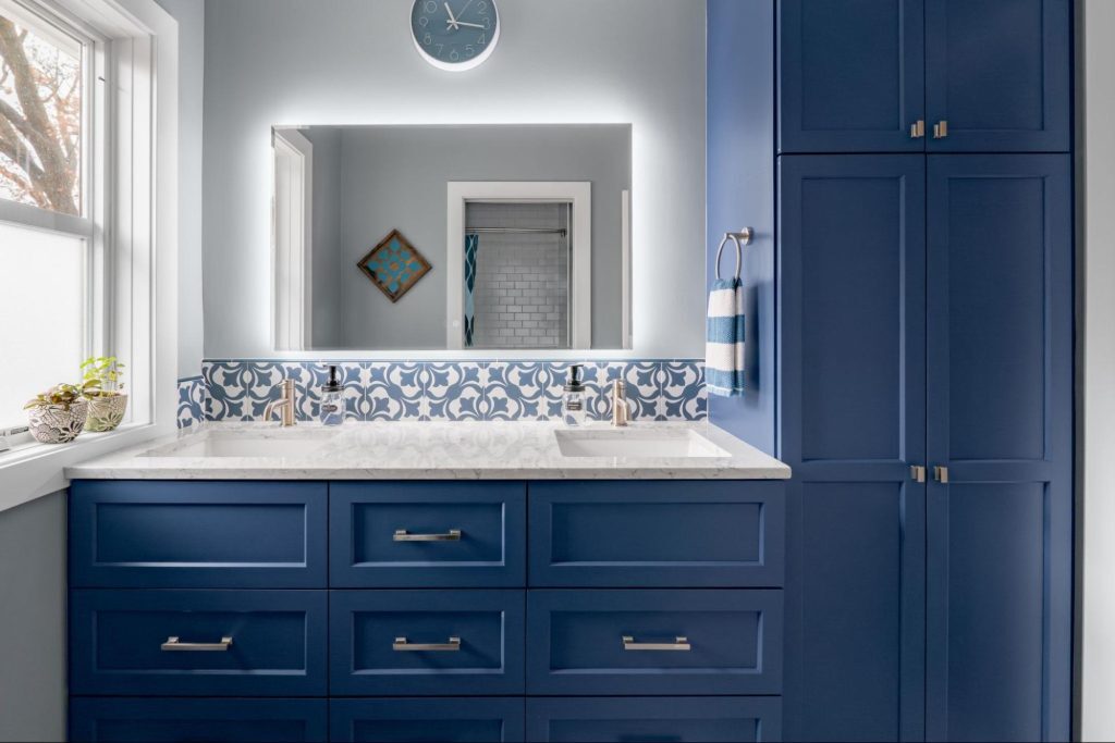 a modern bathroom vanity. bold blue cabinets provide ample storage. the mirror is lit by backlighting.