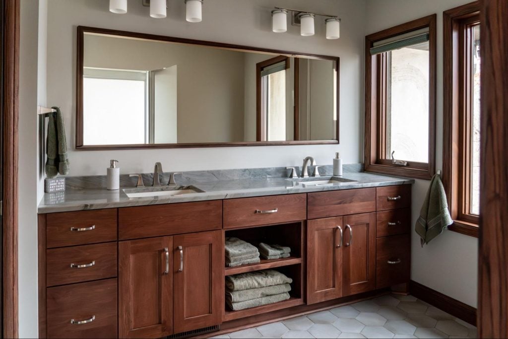 a bathroom with striking wood details. the main sink area is built out warm wooden cabinets that match the trim on the windows and walls.