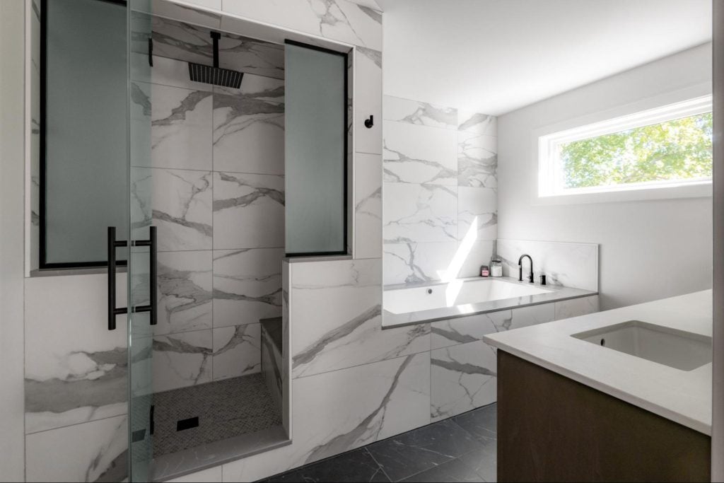 a luxurious bathroom with modern touches. a separate bathtub and shower are both tiled with large-scale marbled white tiles. the floor is lined with large-scale black tiles.