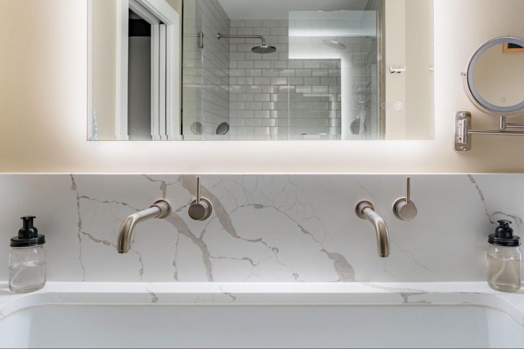 a close-up of a modern vanity area in the bathroom. a smart mirror with touch technology controls the backlight behind the mirror.