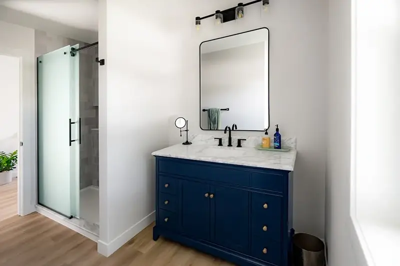 Minnesota bathroom remodel with navy blue vanity, marble countertop, black hardware, and frosted glass shower