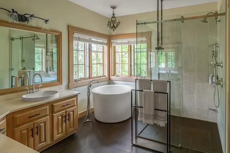 Minnesota primary bathroom remodel with round freestanding tub, bay window, and frameless glass shower enclosure