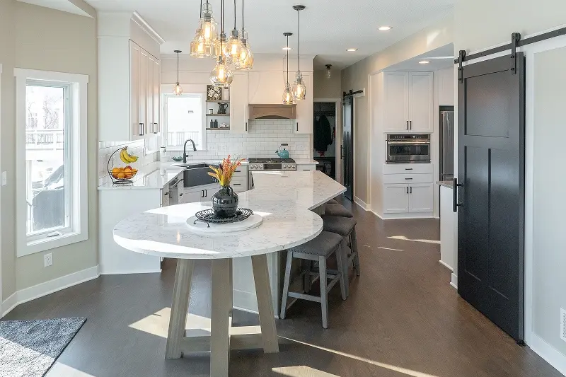 Minnesota kitchen remodel with white shaker cabinets, round marble island, cluster pendant lights, and black barn door