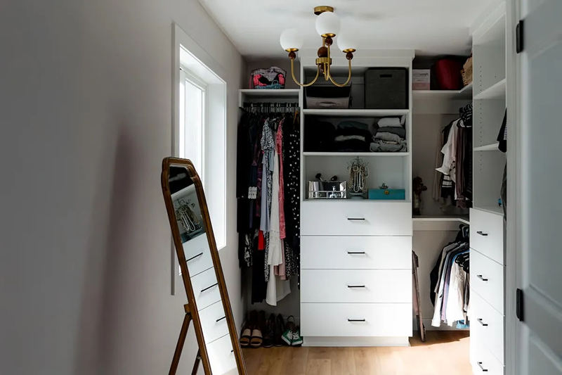 Custom walk-in closet with white built-in shelving, dual hanging sections, and brass chandelier in a Minnesota home remodel