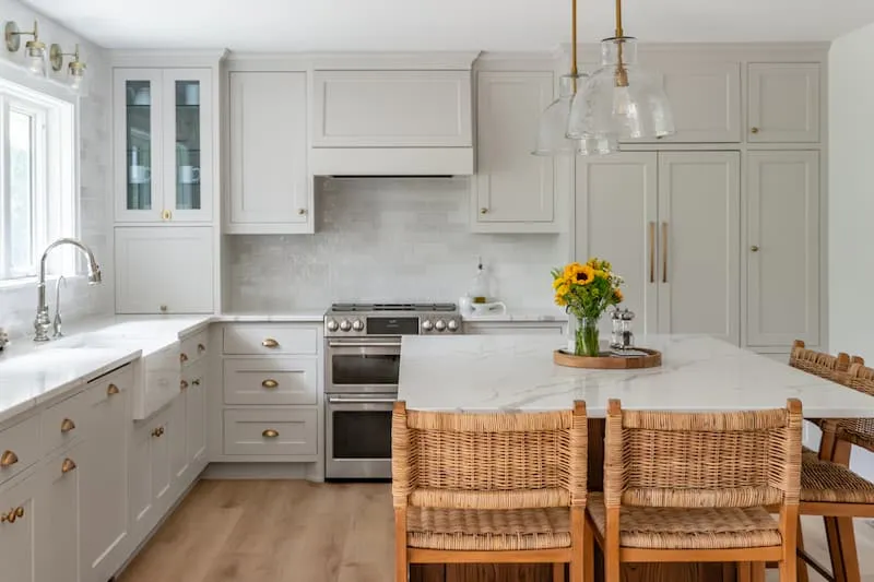 Minnesota kitchen remodel with light gray shaker cabinets, marble countertops, brass hardware, and wicker island seating