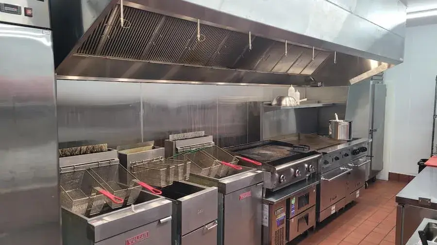 interior of a commercial kitchen, with a row of deep fryers and stovetops