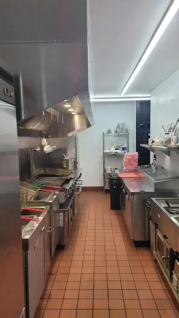 interior of a commercial kitchen, with a row of deep fryers and stovetops
