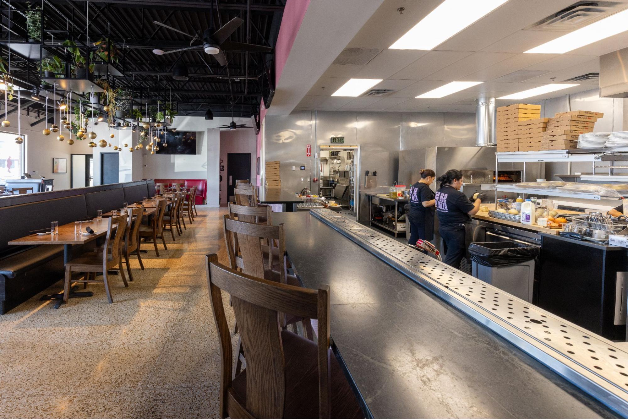 Restaurant interior with bar seating, dining area, and open kitchen where staff prepare food
