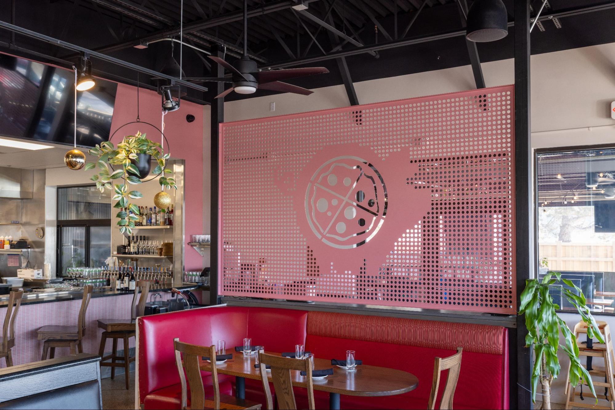 Restaurant interior with red booth seating, bar area, hanging plants, and pink perforated divider with pig ate my pizza logo
