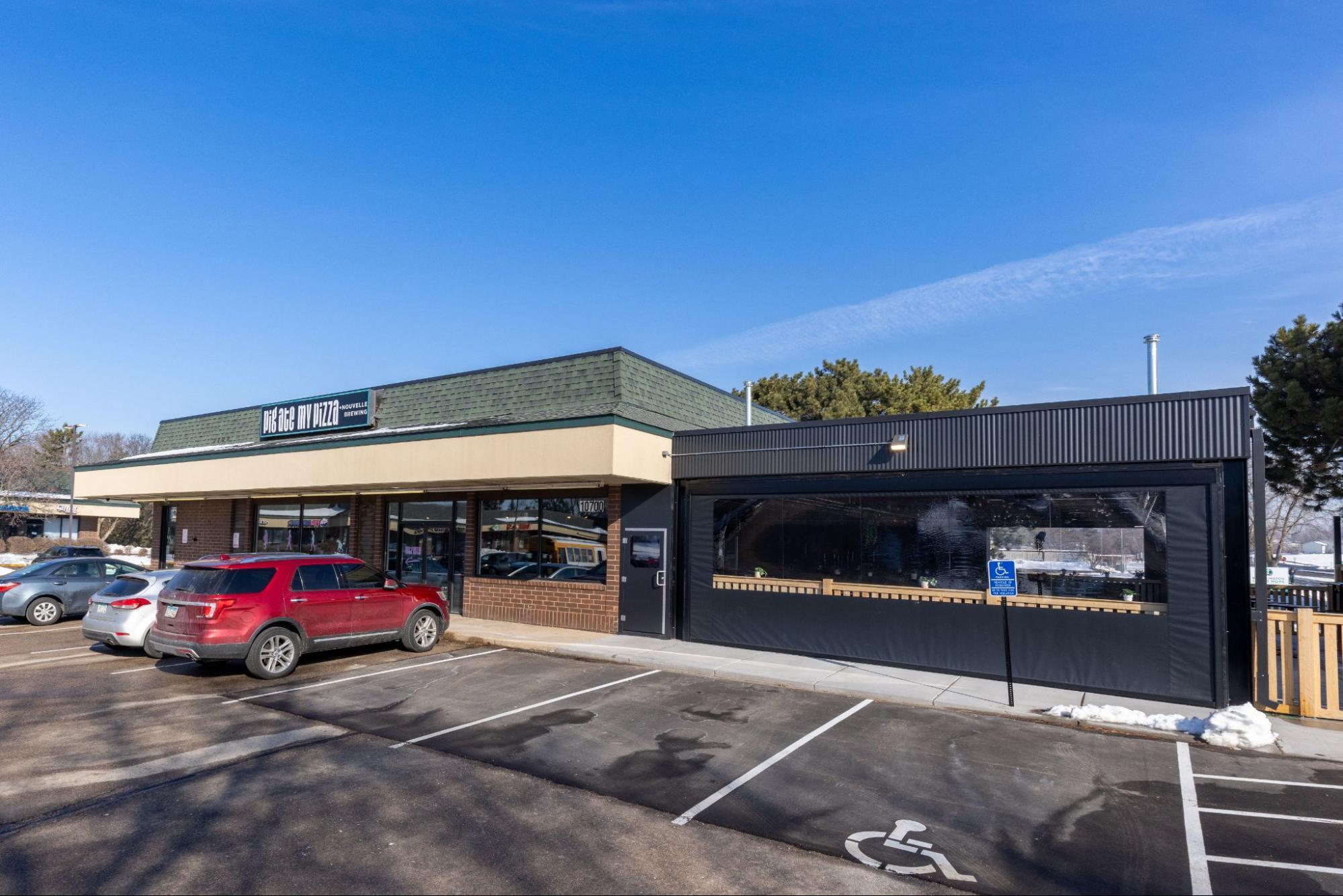 Pig Ate My Pizza restaurant exterior with parking lot, storefront windows, and covered patio enclosure on a clear day