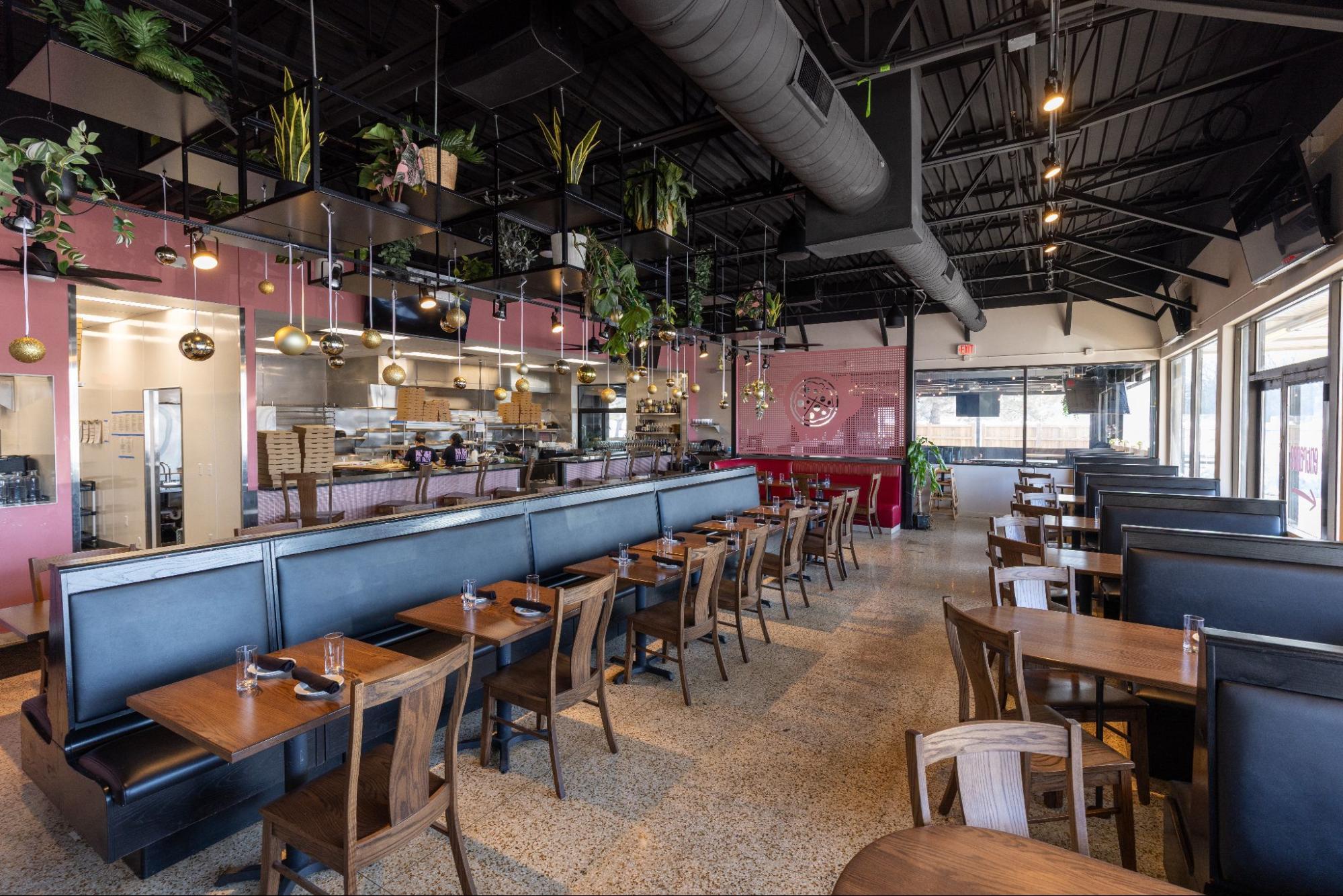 Modern restaurant dining area with booth seating, open kitchen, and hanging plants with decorative lighting
