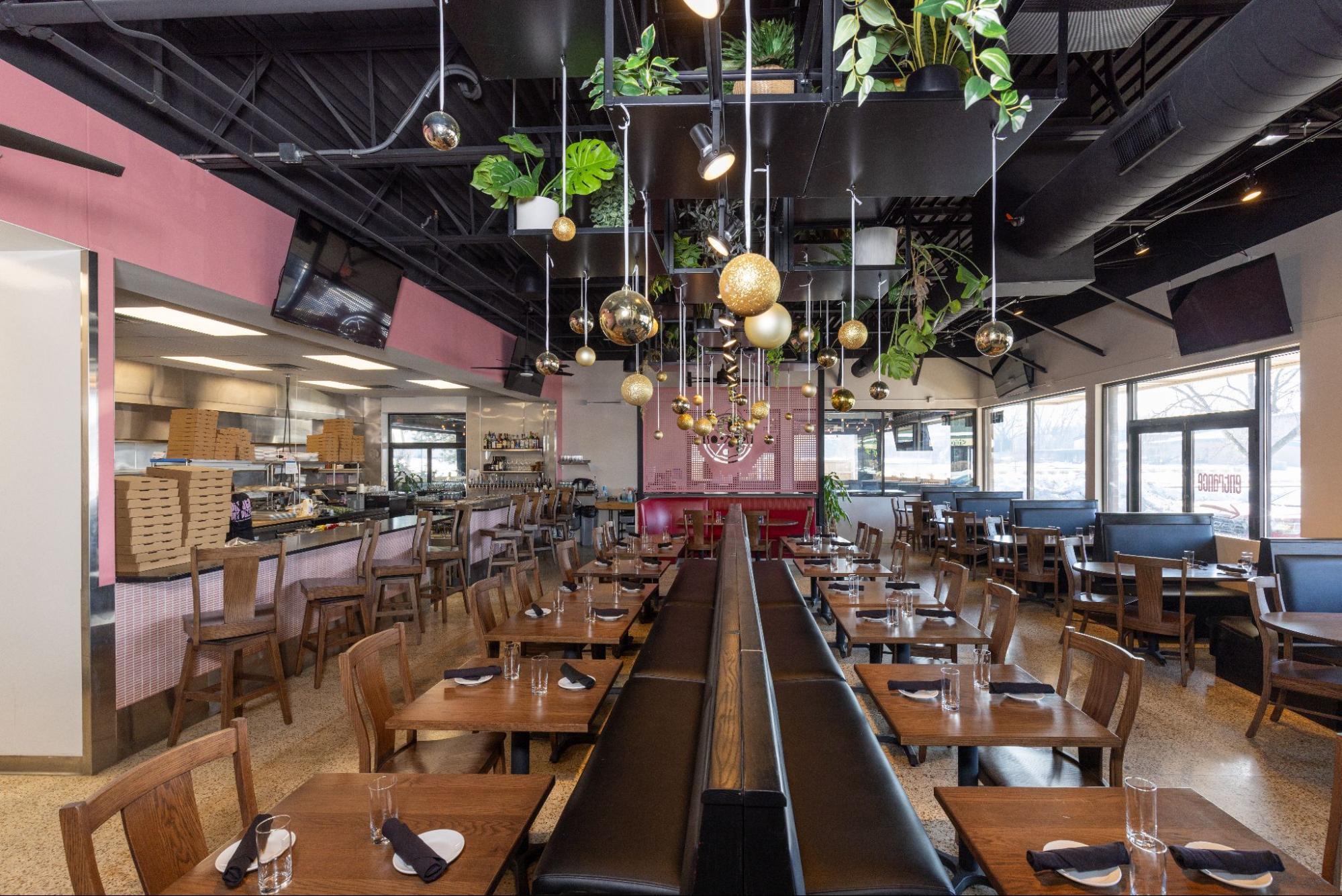 Spacious restaurant dining area with booth seating, open kitchen, and hanging plants with decorative lighting