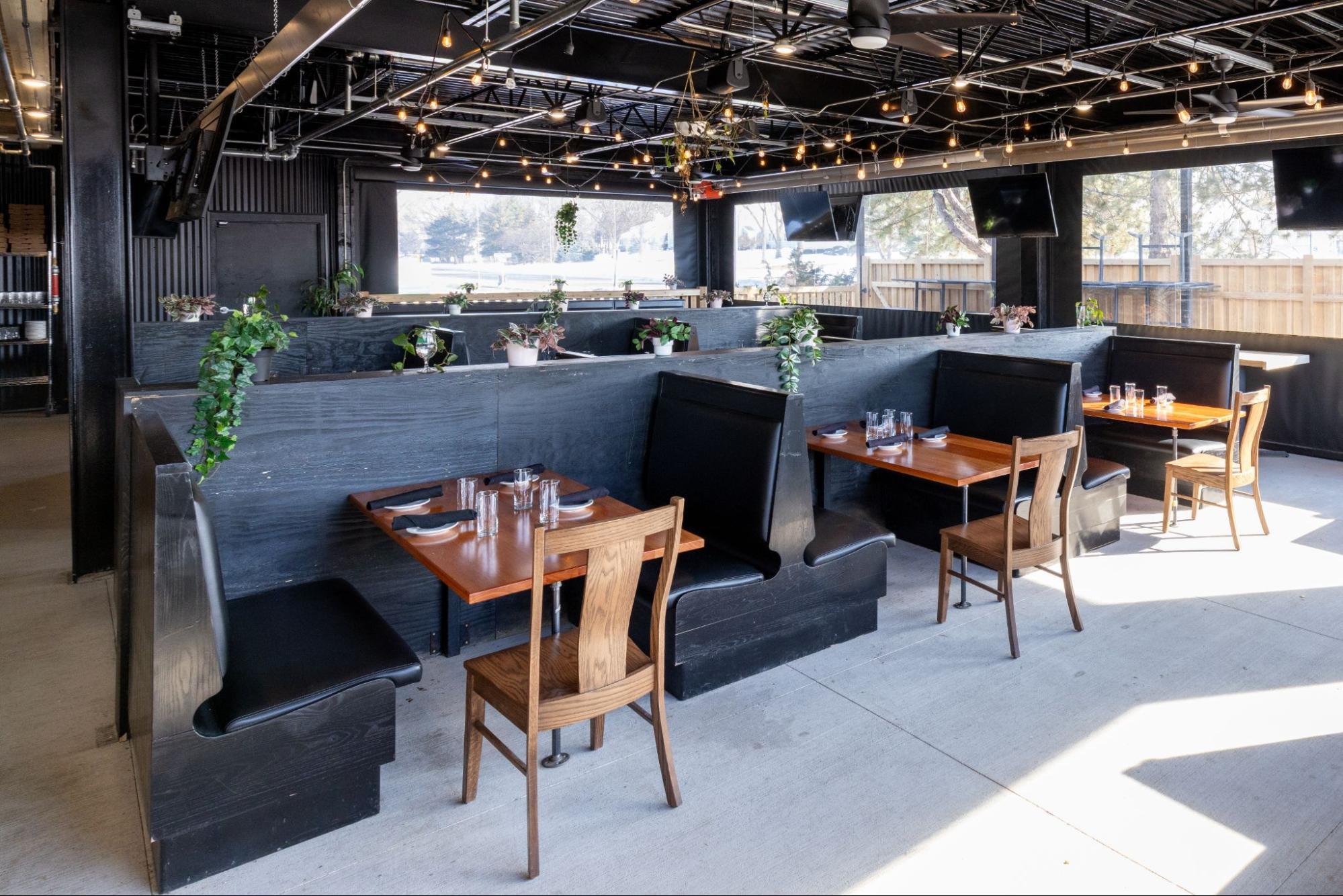 Modern restaurant heated patio interior with booth seating, hanging plants, and decorative lighting near large windows