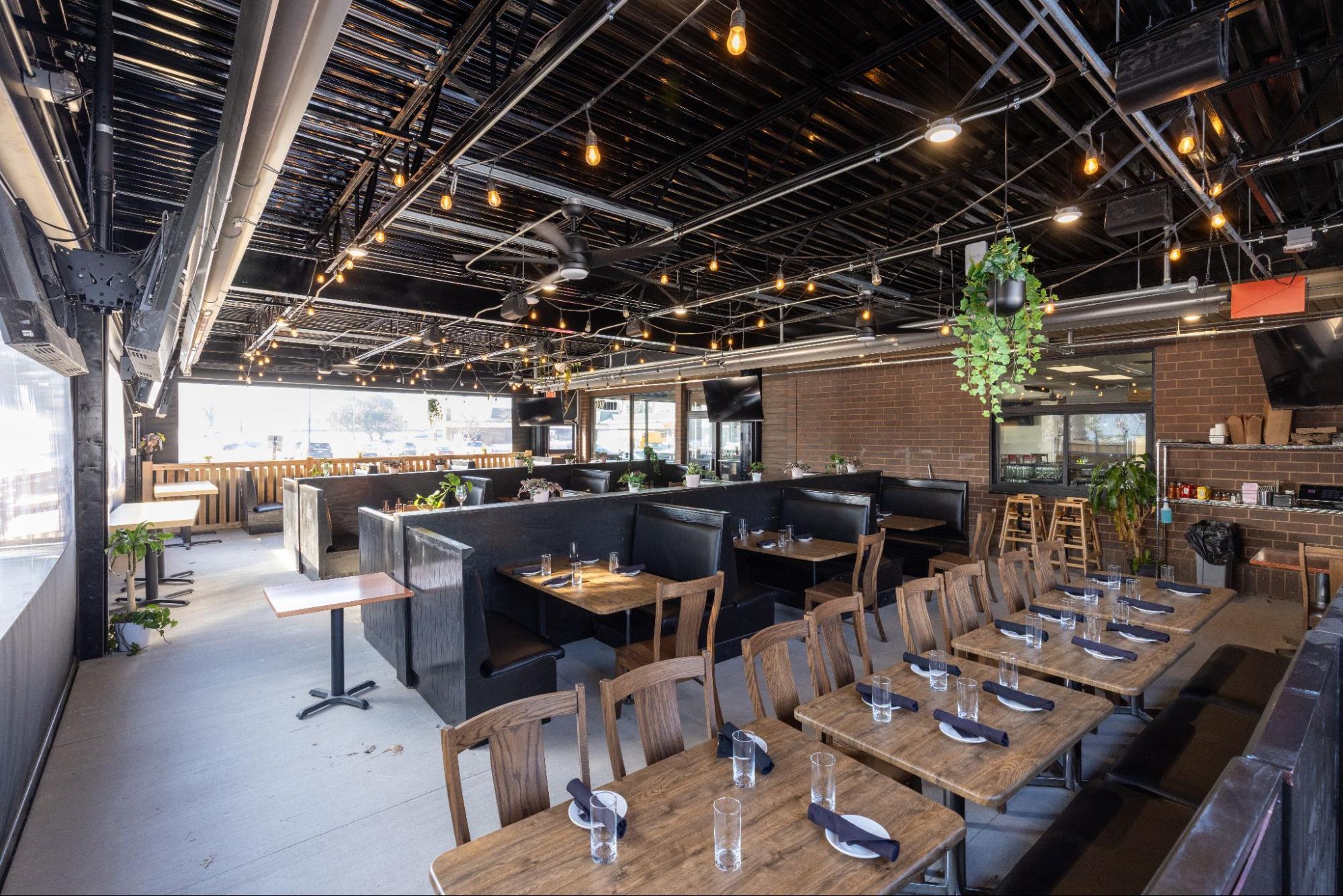 Modern restaurant heated patio interior with booth seating, hanging plants, and decorative lighting near large windows