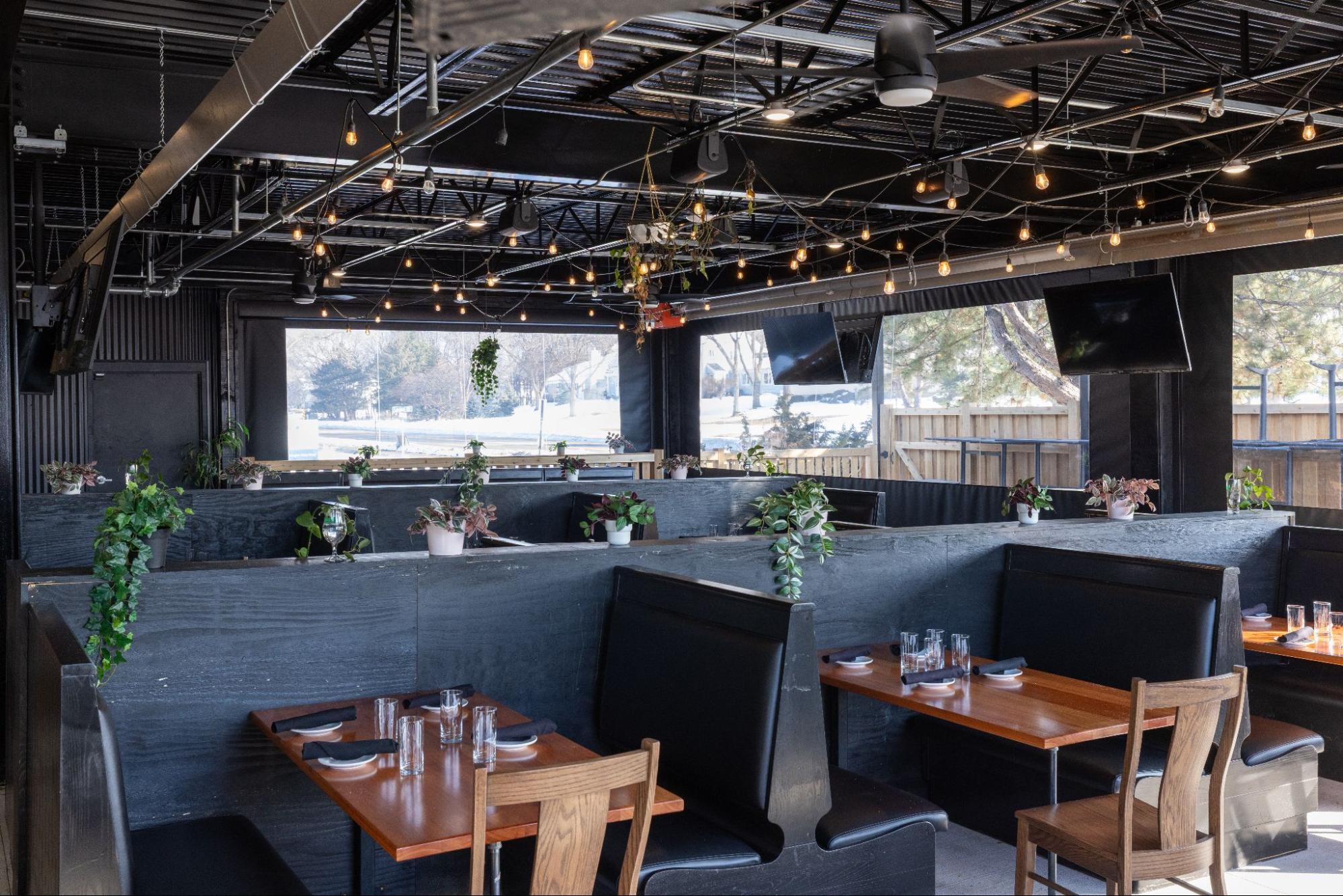 Modern restaurant heated patio interior with booth seating, hanging plants, and decorative lighting near large windows