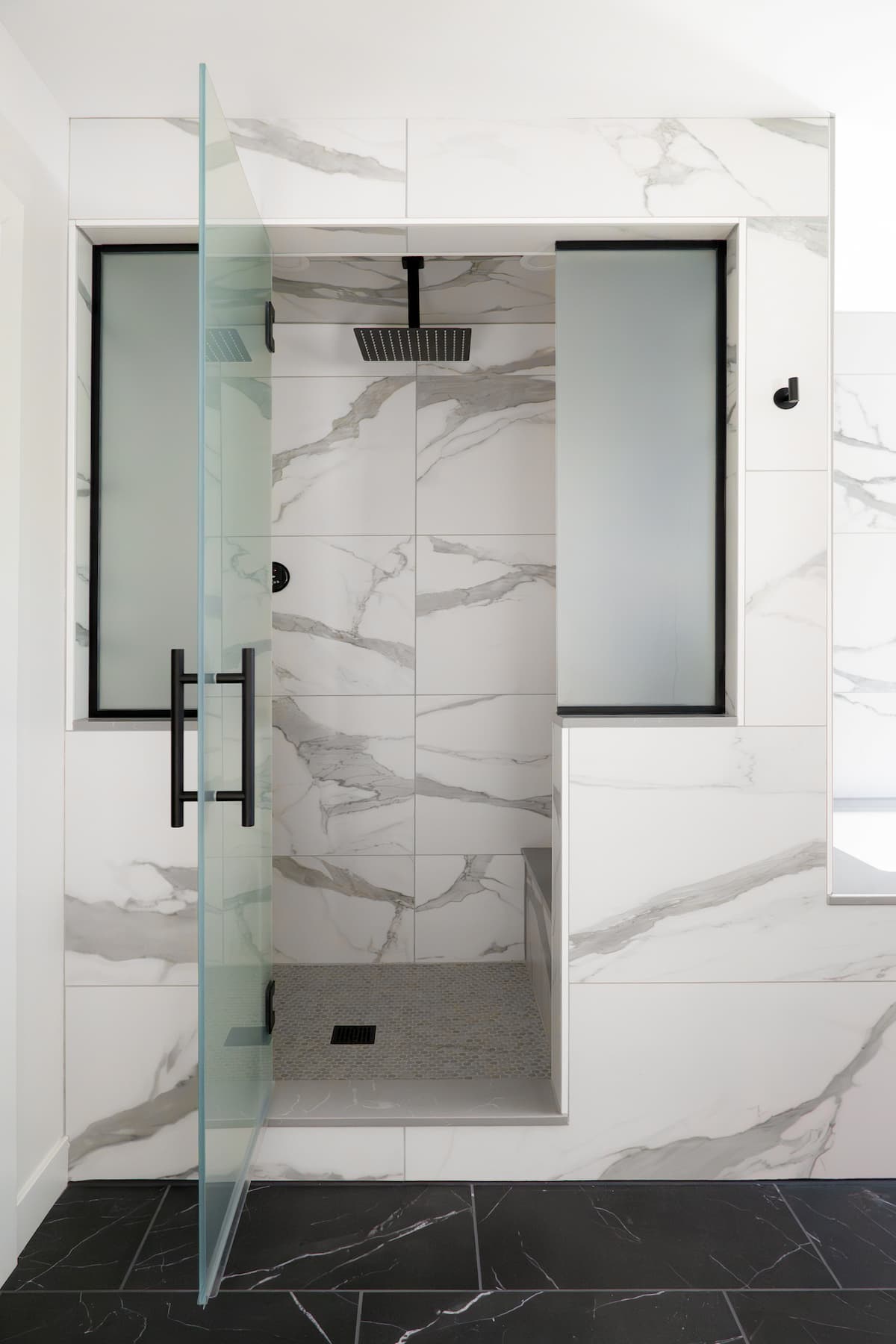 view into private shower, featuring a bench, rainfall showerhead, and large-scale marble-inspired tiling