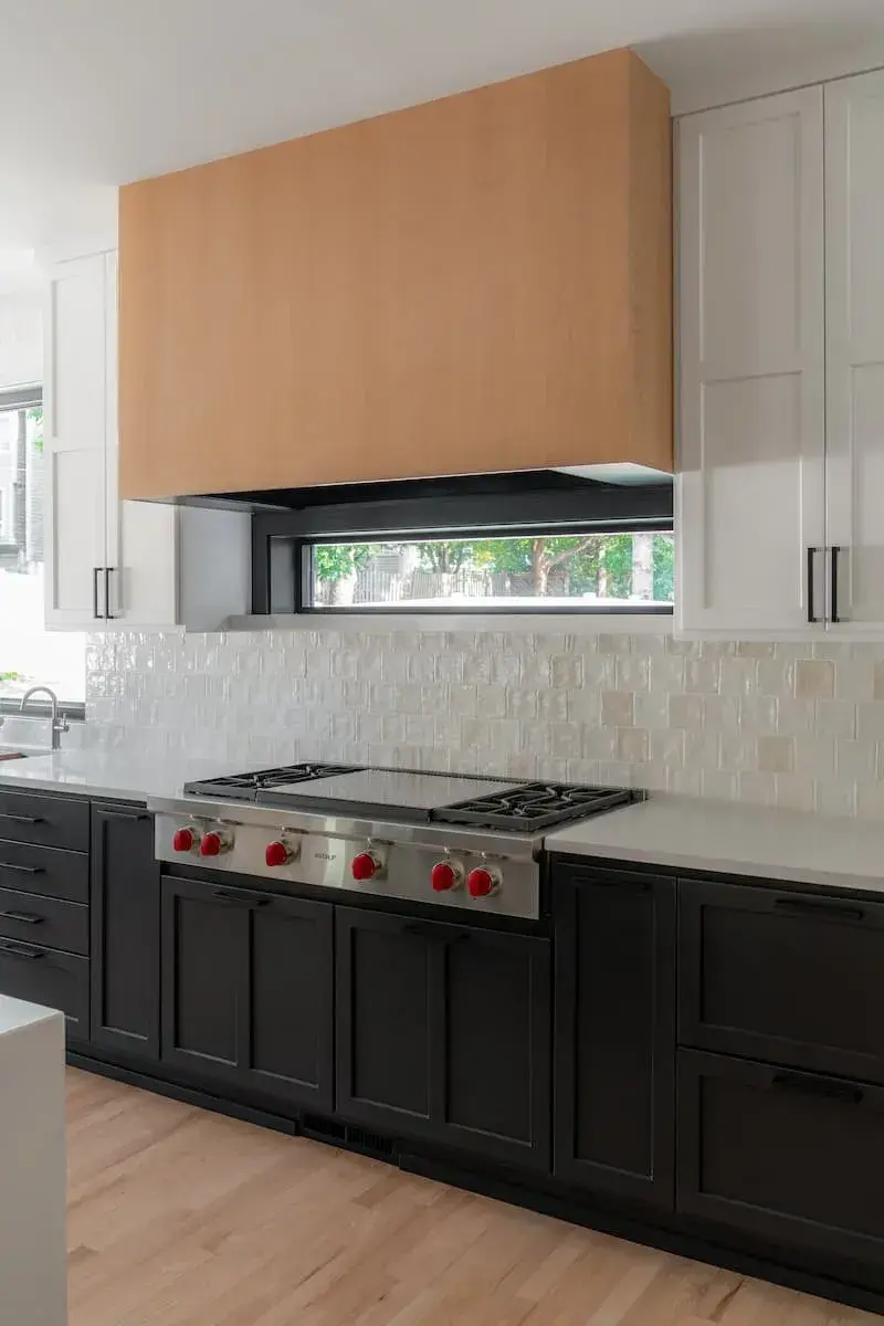Black lower cabinets with white uppers. Wood hood on large wolf range.