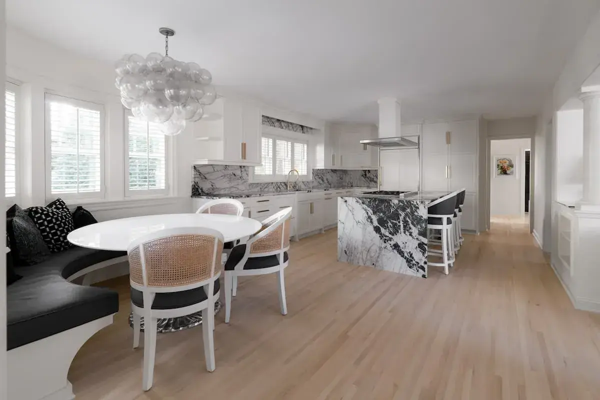 a kitchen and dining area with an open concept plan. the dining area has a built-in bench. The kitchen has striking, black-and-white marbled countertops.