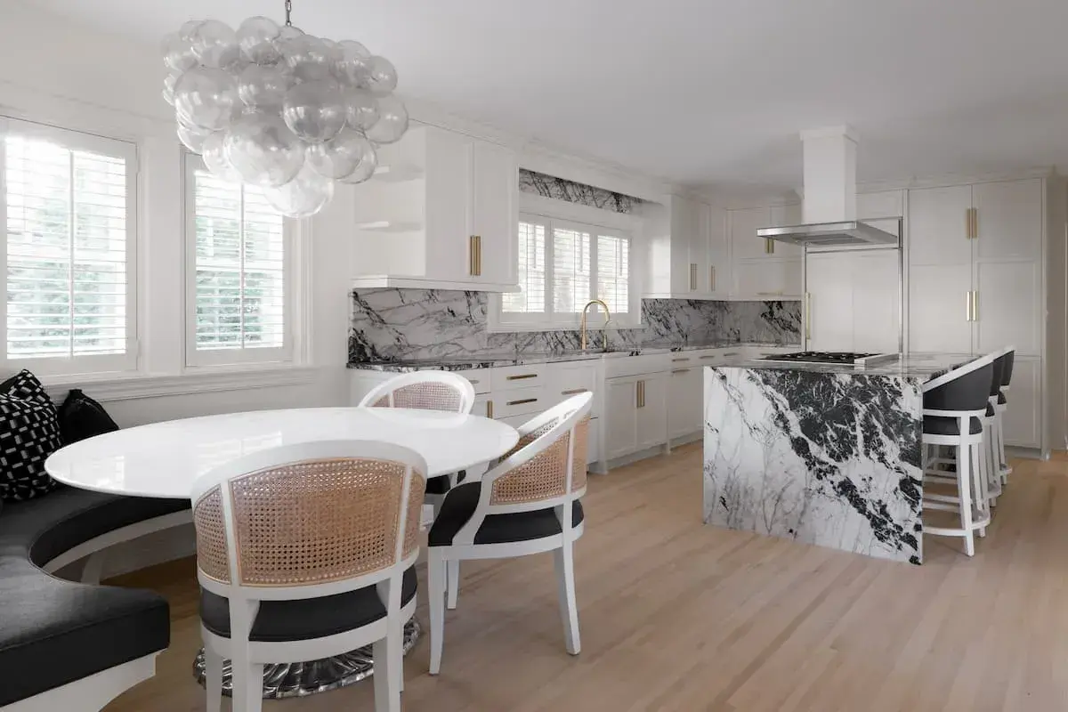 a kitchen and dining area with an open concept plan. the dining area has a built-in bench. The kitchen has striking, black-and-white marbled countertops.