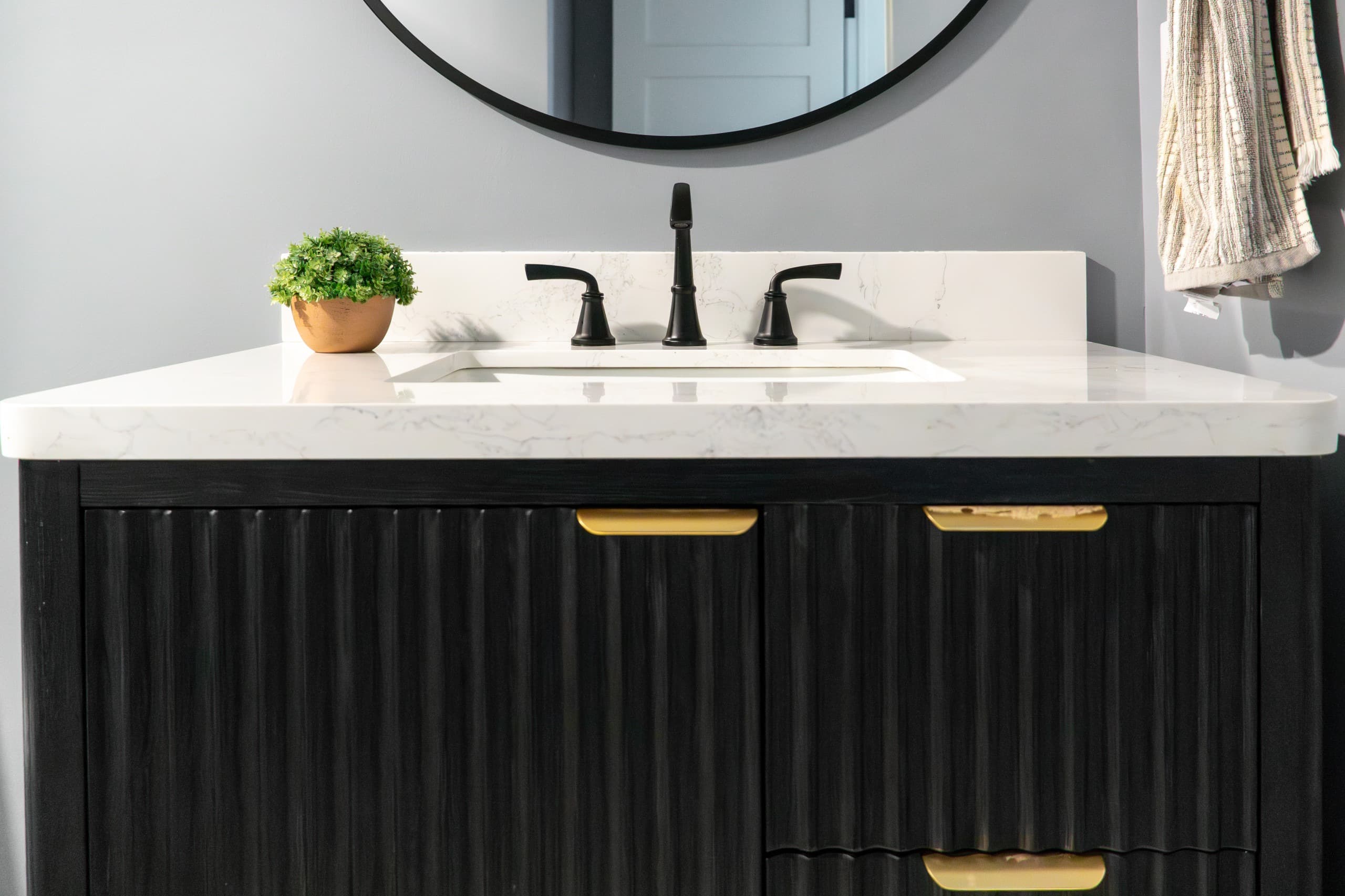 a close-up of a sink vanity with textured cabinet and golden pulls