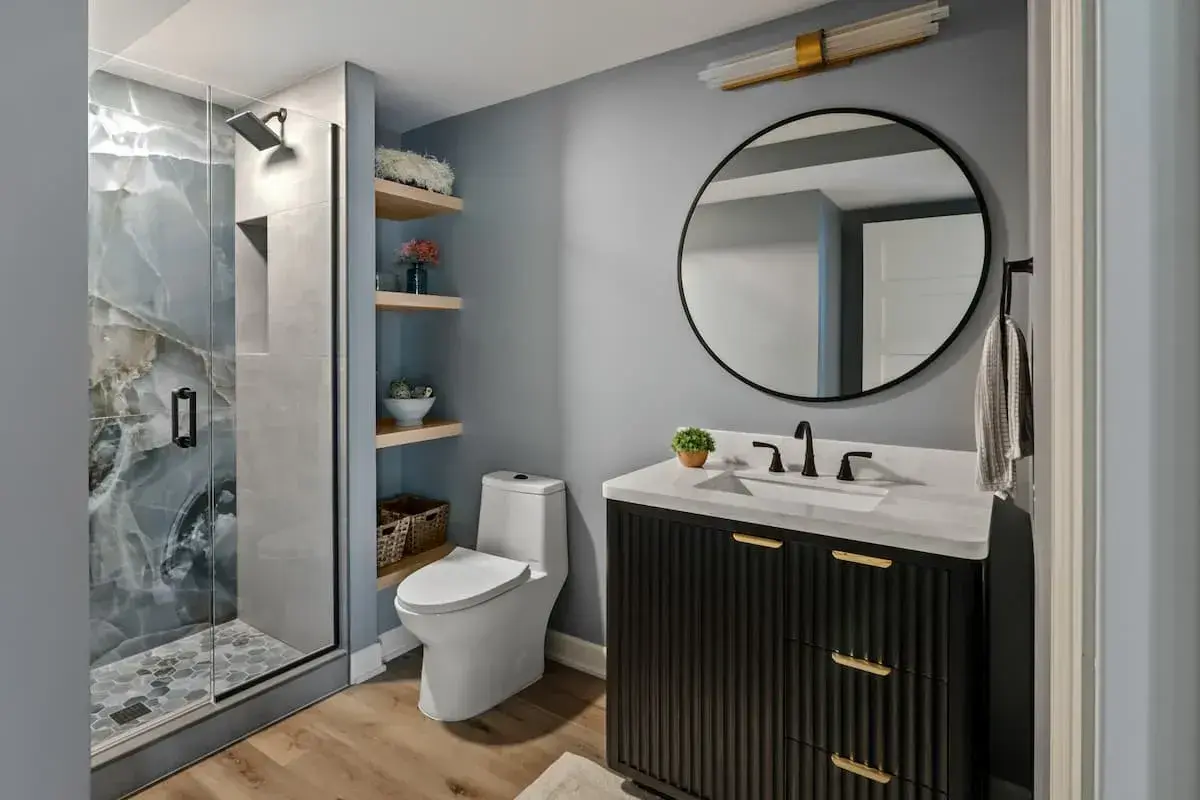 scalloped black vanity with gold hardware and large round mirror. Built in open shelving