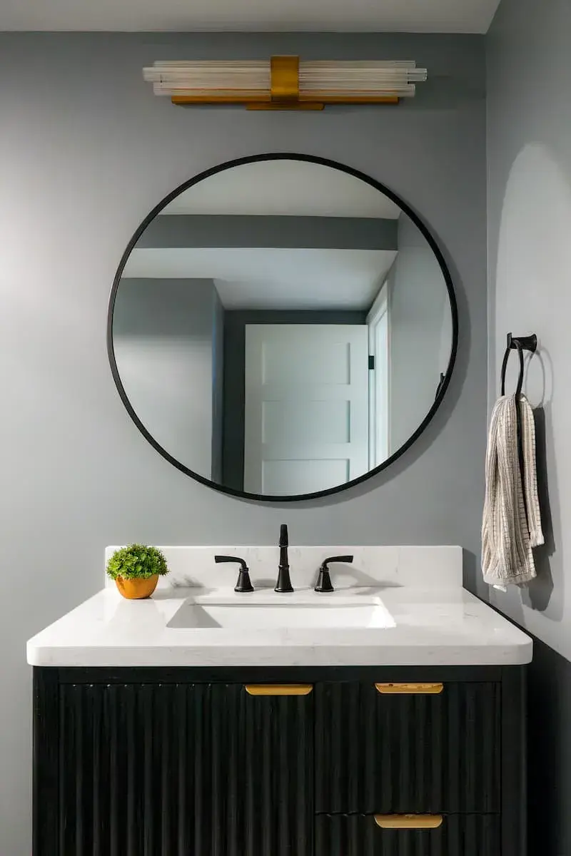 scalloped black vanity with gold hardware and large round mirror