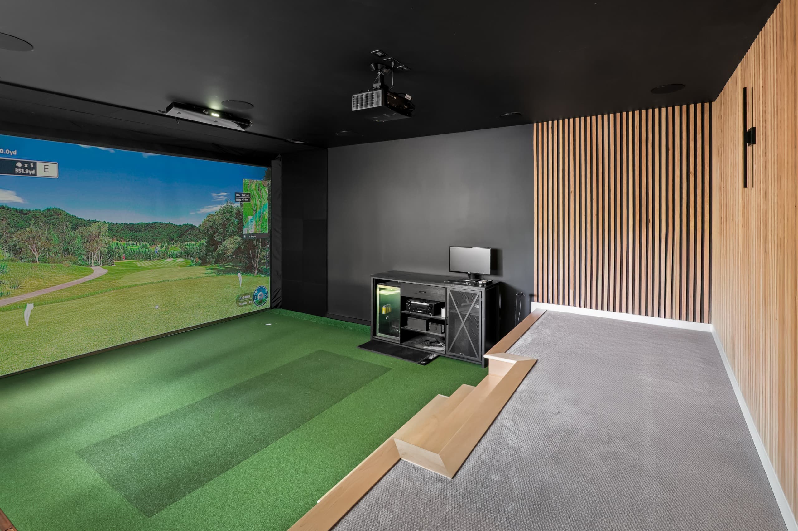 a golf simulator room with green grass and digital screen