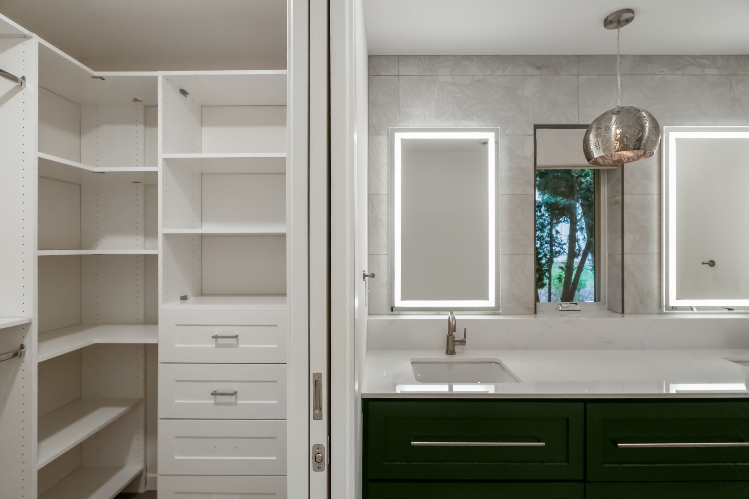 a bathroom with dark green vanity, white countertops, and oversized warm gray stone tiles, and a view into a nearby walk-in closet
