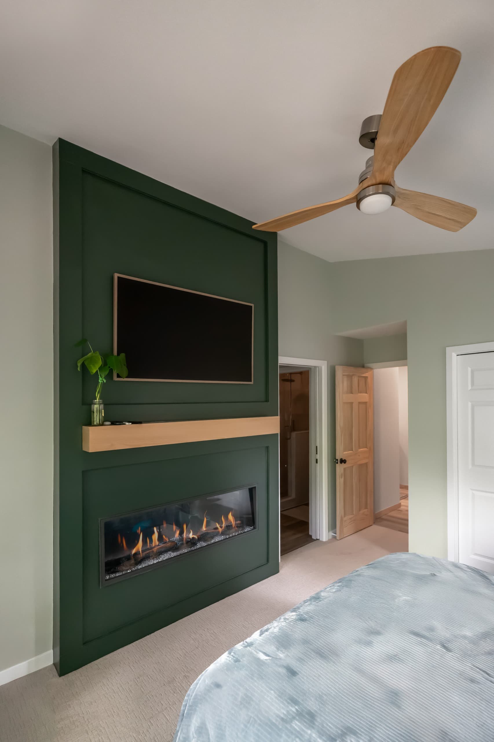 a bedroom with light green walls and a bespoke dark green fireplace/tv built-in