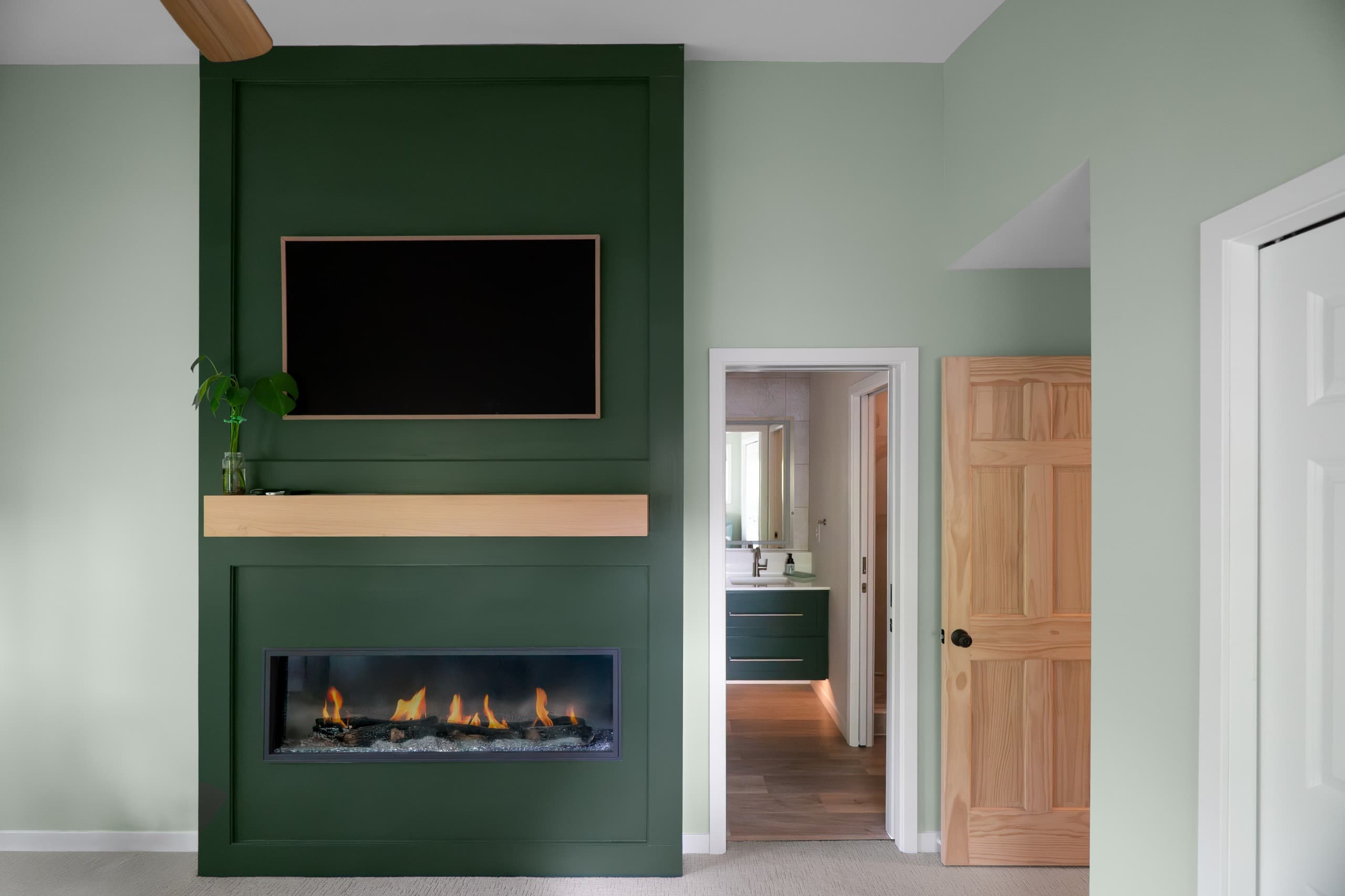 a bedroom with light green walls and a bespoke dark green fireplace/tv built-in